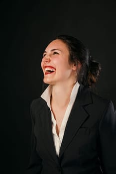 Laughing woman in black business outfit against a black background. Clear competence, value, and vivid beauty. Enjoying a joyful moment, shes ready to face life's challenges again, responsible for