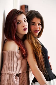 Friends pose with intention. One exudes a laid-back style, the other contrasts with a poofy skirt. Their makeup and thigh-highs accentuate youth they relish momentarily