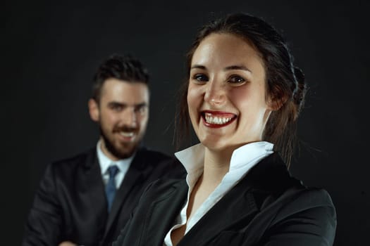 On a dark background, a sharp, prominent woman and a blurred, bearded man, both elegantly dressed in black business attire, epitomize professional assistance in various fields