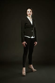 woman in a black suit stands proudly against a black background. Choosing high heels not for male approval, but for her own self-recognition of beauty
