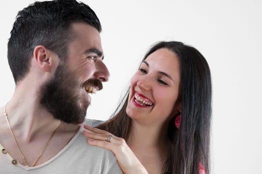 Embracing joyfully, almost posing for holiday pictures. Young bearded man and his girlfriend laugh, her long black hair, earrings, and red lipstick highlighting her beauty