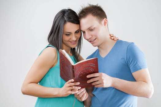 Couple with baby on the way peruse a book. They're engaged in name-choosing, cherishing traditions, and admiring early ultrasound pictures saved for their child