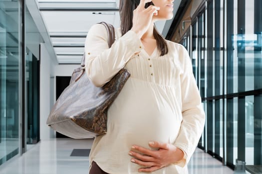 unrecognizable pregnant woman is engrossed in a phone conversation in a corporate environment. Working late into pregnancy, out of necessity or personal commitment and conviction