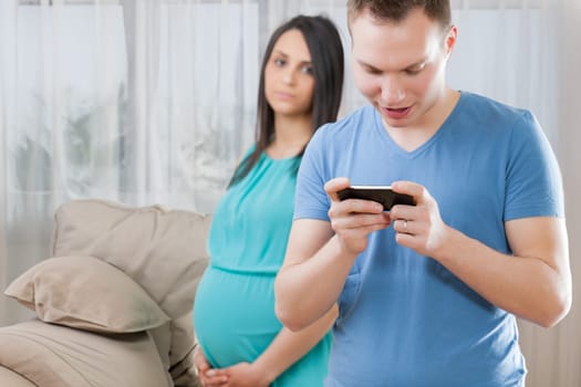 Pregnant young woman observes a man engrossed in games on his phone, reflecting the important responsibility of choosing a partner and creating a life amid limited experience