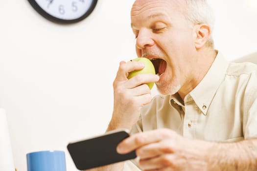 The focus is on a green apple. As the elderly prankster enjoys every drop of its vitamins in his kitchen, he recalls the proverb and his commitment to quality fruit