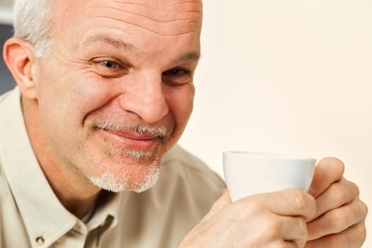 Amidst his thoughts, an aged man tries not to laugh. Holding a drink, likely coffee or tea, he's amused by the notion of something naive or laughable. His seasoned life offers such perspective