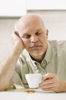 Elderly man, weary from awakening, struggles with his morning coffee. Sleep deprivation impacts his job. Retirement age rises but not his salary. Medical aid for sleep and reduced stress is crucial