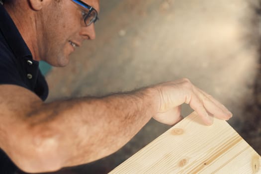 The carpenter, wearing glasses, is hard at work assembling a furniture piece he crafted by hand. He must be precise, strong, and minimize risks. These skills make the product valuable