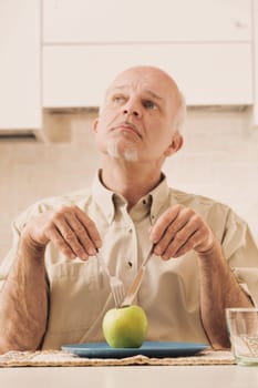 With only a green apple on his plate, an elderly man readies himself, making funny faces. Beneath this facade, he craves delicious foods filled with fats, sugars, and carbs. The doctor's advice? Such