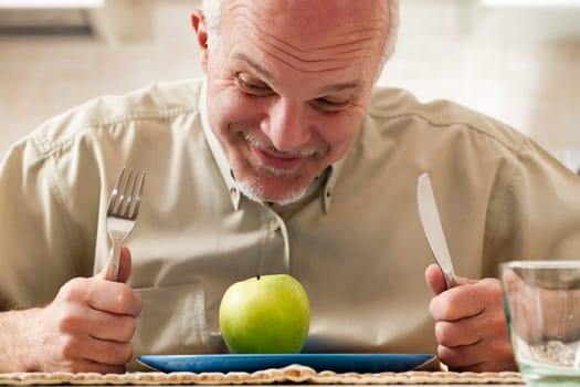 old man stoically prepares to eat just a green apple. It's the only item on his plate, with utensils on the side. His humorous expressions mask a deep desire for rich, fatty, sugary, salty, and carby