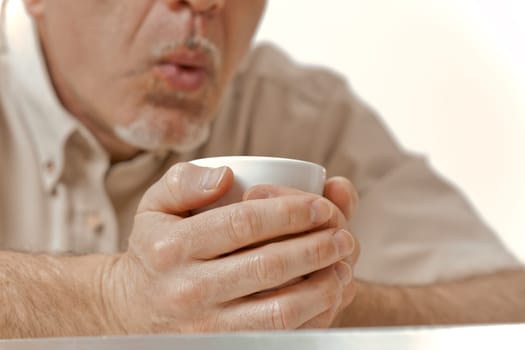 Amidst the cold embrace of a winter morning, the sun offers little relief. An aged man with an unrecognizable face tightly holds his coffee, blowing on it to cool. It's a delicate balance between warm