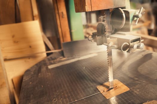 Wide-angle view of an upright bandsaw with its table top ready with sharp, pointed teeth to bite into wood. The warm colors of the craft workshop.