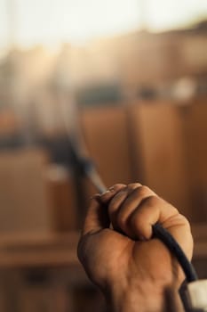 A strong male hand is in focus as it grips and pulls a thick electrical cable towards a blurry background. The hand is dirty from physical artisanal or labor work, and the colors are warm