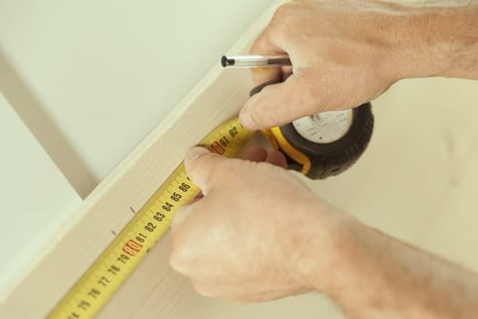Close-up detail of a carpenter's tape measure as he measures a piece of wood that he will later use in his woodworking workshop