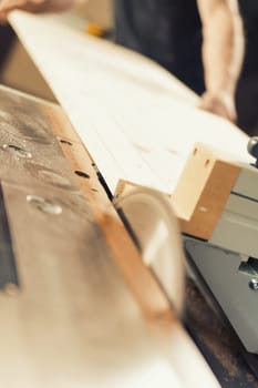 Strong carpenter's hands hold, guide, restrain, push, and move lumber while working with powerful cutting machines in his workshop. Image conveys strength, skill, and risk-taking expertise