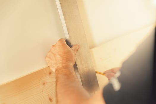 A wood artisan traces lines and takes measurements in his brightly lit woodworking shop. He is focused and skilled, his expertise is all personal and manual, using tools with mastery