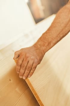 The strong hand of a man lifts a large wooden board with force and precision. The focus is on the hand, while the rest is in selective blur