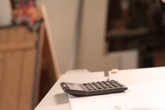 calculator in the foreground resting on a table full of papers, the rest is blurry, the calculator is all smeared with sawdust