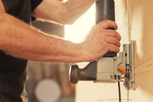 Carpenter's hands with tool vertically cutting wood, backlighting and strong arms