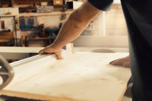 In sharp focus, the woodworker's hands carefully position, insert, and fix components of handmade furniture in his workshop. He thinks before he acts with skill and determination. The background is bl