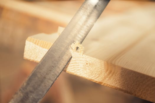 Detail of a hand-cutting blade notching the first corners of a board, obtaining wood curls and bevels in the surface, often intentionally irregular. Wood craftsmanship.