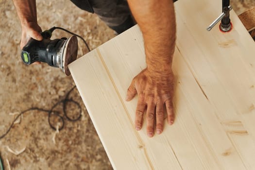 Carpenter at work with a modern sander. A small tool that moves sandpaper at high speed with the precision and control the craftsman wishes to impart. Details of hands at work and the wood.