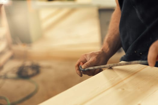 The artisan carves and chamfers the edges of the wooden boards that make up the furniture with a drawknife. Strong male hands and wood are visible, embodying the essence of carpentry