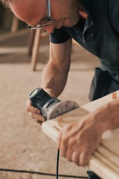 Carpenter at work with a modern sander. A small tool that moves sandpaper at high speed with the precision and control the craftsman wishes to impart. Details of hands at work and the wood.