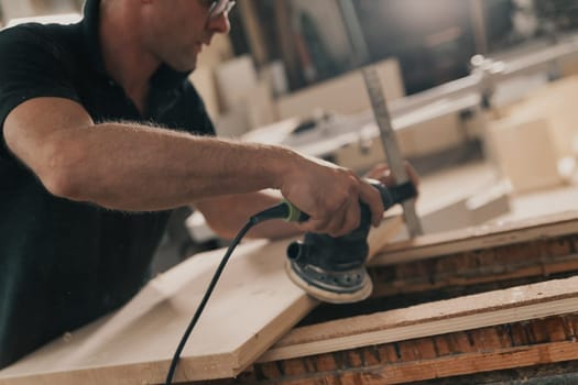Carpenter at work with a modern sander. A small tool that moves sandpaper at high speed with the precision and control the craftsman wishes to impart. Details of hands at work and the wood.