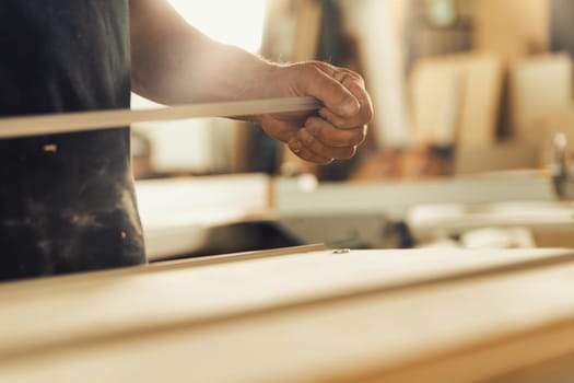 Concept of waiting and observing while planning the work. Carpenter's strong hands hold a bar of some sort, with a tiny detail he's focusing on in sharp focus, blurring most of the workshop
