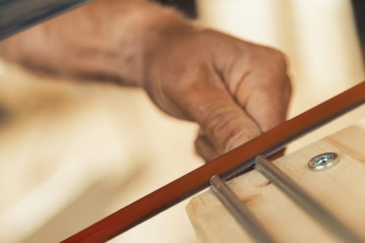 With extreme precision, the carpenter stops the hand saw with his thumbnail and index finger to work on aluminum inserts that will help drawers glide smoothly. The details are in sharp focus, while th