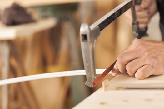 Precision cutting made by a carpenter with a hand saw on a small metal component of a piece of furniture. In a risky operation requiring skill he cuts by holding with one hand.