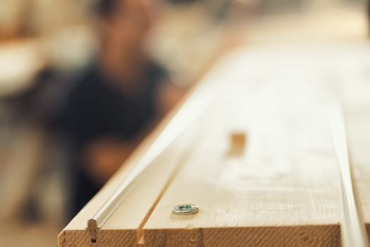 A very shallow depth of field highlights the details of a semi-finished wooden board, with carvings, metal inserts, and tracks that will become part of a piece of furniture made by an artisan carpente