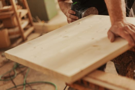 Carpenter at work with a modern sander. A small tool that moves sandpaper at high speed with the precision and control the craftsman wishes to impart. Details of hands at work and the wood.