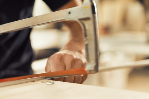 With extreme precision, the carpenter stops the hand saw with his thumbnail and index finger to work on aluminum inserts that will help drawers glide smoothly. The details are in sharp focus, while th