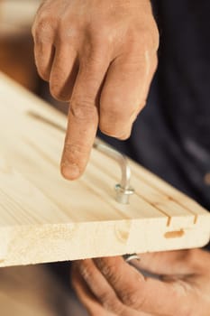 The carpenter screws and secures a wooden board using an Allen key, holding the other side with one hand. Strong, muscular, and hairy arms and hands are visible, exemplifying the manual labor involved