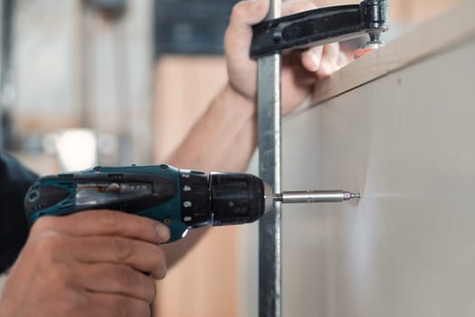In focus: cordless drill-driver with built-in LED light in the hands of an experienced carpenter. He is located in his own workshop and uses every necessary tool.