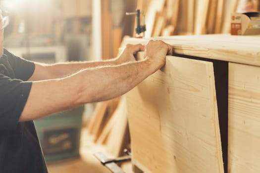 Strong carpenter's hands hold, guide, restrain, push, and move lumber while working with powerful cutting machines in his workshop. Image conveys strength, skill, and risk-taking expertise
