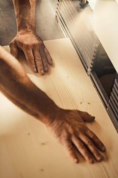 Strong carpenter's hands hold, guide, restrain, push, and move lumber while working with powerful cutting machines in his workshop. Image conveys strength, skill, and risk-taking expertise