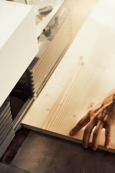 Strong carpenter's hands hold, guide, restrain, push, and move lumber while working with powerful cutting machines in his workshop. Image conveys strength, skill, and risk-taking expertise