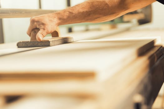 The professional woodworker uses a modern planer or sander with a manual component. He works with ease but applies effort where necessary, shown here smoothing long planks on a large machine