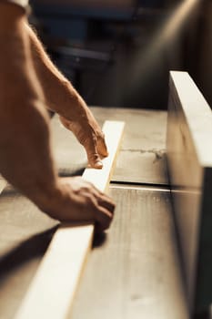 The strong and muscular hand and forearm of a carpenter holding a metal tool, using it to aid in the construction of a piece of furniture that will be entirely crafted by him. The warm sunlight floodi