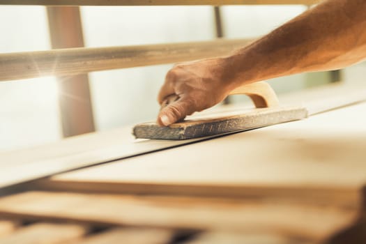 The professional woodworker uses a modern planer or sander with a manual component. He works with ease but applies effort where necessary, shown here smoothing long planks on a large machine