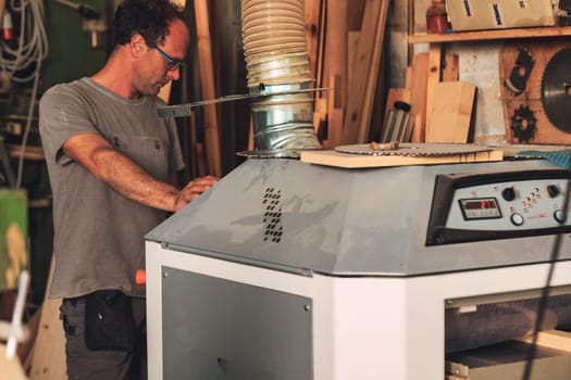 Carpenter in a messy corner of the woodshop, with lots of lumber, working with a large machine equipped with a powerful fume hood. Safety first.