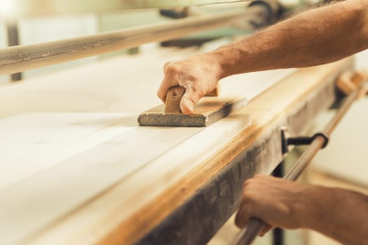 The professional woodworker uses a modern planer or sander with a manual component. He works with ease but applies effort where necessary, shown here smoothing long planks on a large machine