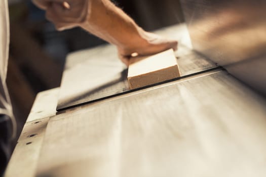 The strong and muscular hand and forearm of a carpenter holding a metal tool, using it to aid in the construction of a piece of furniture that will be entirely crafted by him. The warm sunlight floodi