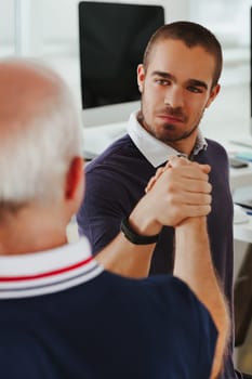Young man in a navy polo exudes confidence during an arm-wrestled handshake with an elder on the job