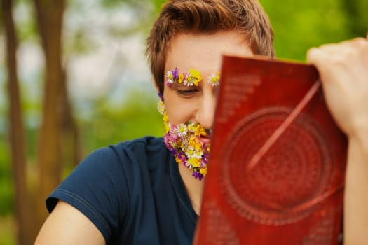 The woods envelop a man whose face, rather unusually, is adorned with floral beauty. He finds solace reading a classic leather book