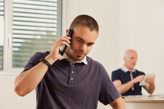 Office scene where a young professional takes a call, another person working in the background