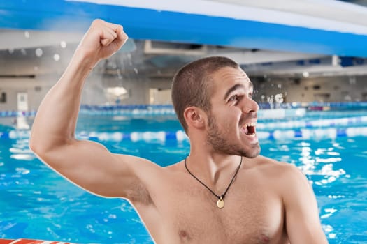 Exuberant young man celebrates triumph at an indoor swimming pool